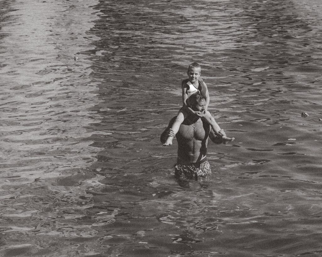 Father carrying his child through the sea during a destination wedding weekend in Europe.